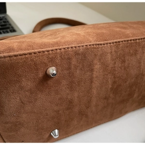 Detail view of silver metal feet and stitching on the brown suede tote bag base
