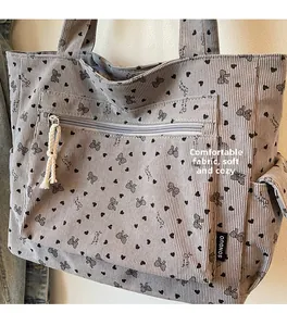 Detail of grey corduroy tote bag showing black heart patterns and front zipper pocket