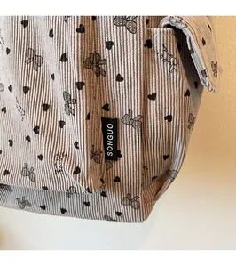 Detail of light gray corduroy tote bag featuring black heart and bow prints and brand tag