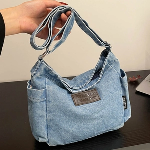 Light blue denim tote bag with brown leather patch and adjustable strap on a wood table