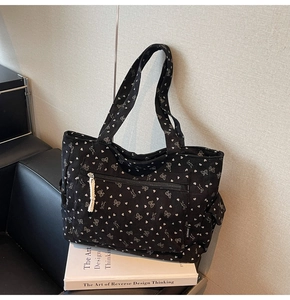 Detail of black corduroy tote bag with white bow pattern and front zipper pocket
