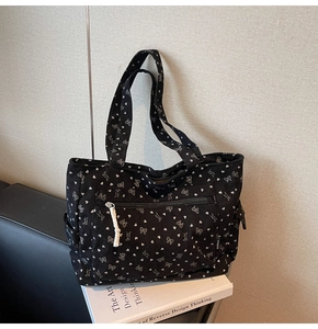 Detail of black corduroy tote bag showing white bow patterns and front zipper pocket