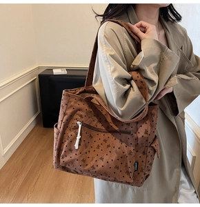 Detail of dark brown corduroy tote bag with heart and bow prints and a zipper pocket