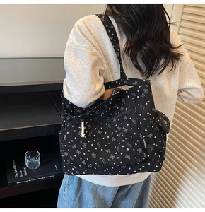Detail of black corduroy tote bag showing side flap pocket and white bow print on the fabric