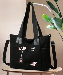 Detail of black corduroy tote bag featuring floral embroidery and adjustable strap