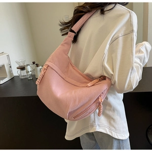 Sac croissant en velours côtelé rose porté par un modèle dans un café chic