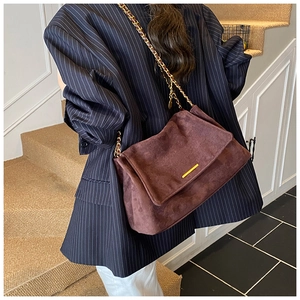 Détail du sac à bandoulière en daim marron foncé avec barre dorée et chaîne sur blazer