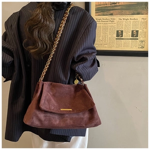 Détail du sac bandoulière en daim marron foncé avec chaîne et ornements dorés