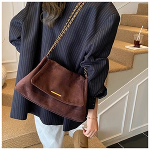 Sac bandoulière en daim marron avec chaîne dorée et détails métalliques en décor moderne