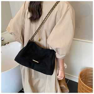 Détail du sac à bandoulière en suède noir avec chaîne dorée et barre métallique