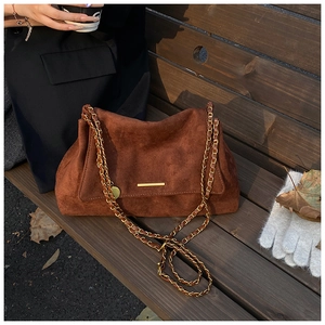 Détail du sac cabas en daim marron avec chaîne dorée et barre en métal sur banc en bois