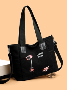 Close-up of black corduroy tote bag showing colorful floral embroidery and striped texture
