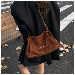Détail d'un sac cabas en daim marron avec chaîne dorée dans un décor de rue automnal