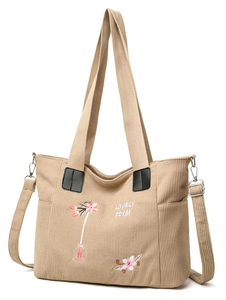 Detail of floral embroidery and text on a beige corduroy tote bag with black leather straps