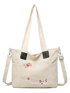 Detail of beige corduroy tote bag featuring floral embroidery and adjustable strap