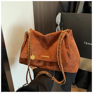 Détail d'un cabas vintage en daim marron rouge avec chaîne dorée et pendentif métallique