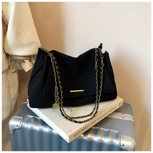 Détail d'un sac en daim noir avec chaîne dorée et fermoir métallique posé sur un livre
