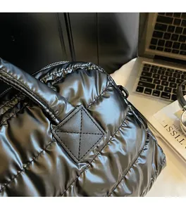 Detail of glossy black quilted puffer bag texture with reinforced strap and modern props