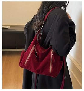 Detail of burgundy suede shoulder bag featuring decorative zippers and functional side pockets