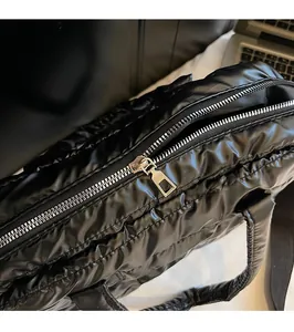 Close-up of the silver metal zipper and quilted puffer fabric texture of the black tote bag