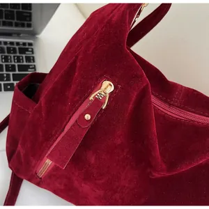 Detailed close-up of a smooth gold metal zipper on a burgundy velvet tote bag texture