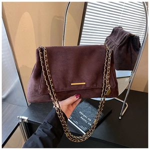 Détail d'un sac cabas en daim marron avec barre dorée et pendentif décoratif en miroir