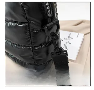 Detail of detachable plastic buckle and woven strap on black shiny puffer tote bag