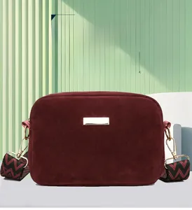 Detail of burgundy suede crossbody bag with golden metal plate and patterned shoulder strap