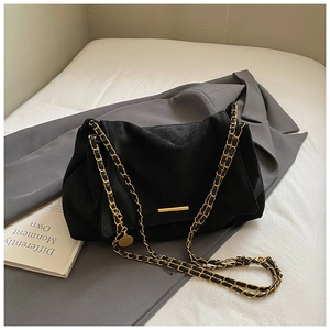 Détail d'un sac bandoulière en daim noir avec boucle dorée et bandoulière en chaîne