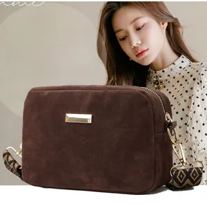 Detail of dark brown suede crossbody bag featuring a wide geometric pattern woven strap