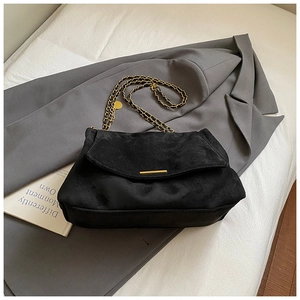 Gros plan sur un sac à rabat en daim noir avec chaîne dorée et détails métalliques
