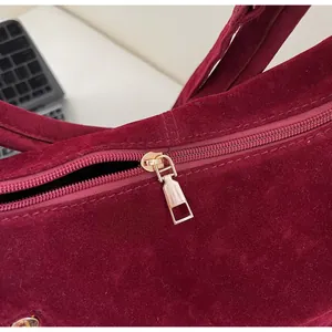 Close-up of a smooth gold metal zipper on a burgundy suede tote bag for women