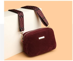 Detail of burgundy frosted camera bag with wide patterned strap and gold hardware