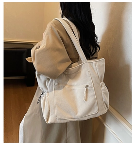 Detail of off-white corduroy tote bag showing side drawstring pocket and strap on shoulder