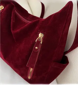 Detailed macro view of the smooth gold metal zipper on a dark red suede tote bag