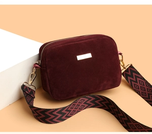 Detail of burgundy suede shoulder bag featuring a wide geometric pattern strap and gold hardware