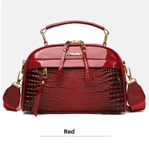 Détail du sac carré rouge foncé à motif crocodile avec lettrage doré et large bandoulière