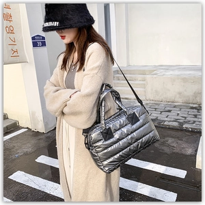 Outdoor view of silver quilted down tote bag with black straps worn crossbody style