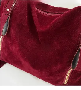 Detail of burgundy velvet tote bag featuring black leather handles and gold metal rivets