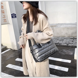 Side view of a metallic silver quilted puffer tote bag with black straps in a city setting