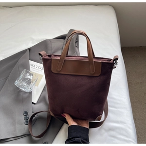 Dettaglio borsa tote in pelle scamosciata viola scuro con manici marroni su sfondo ufficio