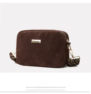 Close-up of brown suede camera bag featuring golden hardware and geometric strap