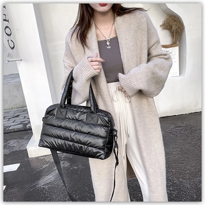 Detail of black quilted puffer tote showing adjustable nylon strap and padded texture