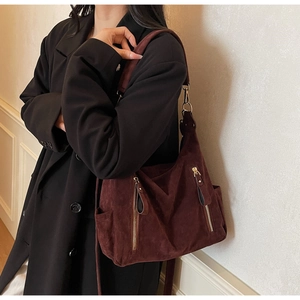 Detail of burgundy suede tote bag with golden zipper on a model in a black wool coat