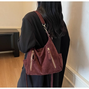 Detail view of burgundy suede tote bag featuring golden zippers and adjustable shoulder strap