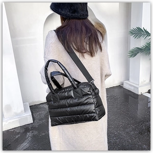 Detail of black quilted puffer tote bag with padded handles and wide nylon shoulder strap