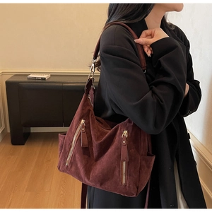 Detail of burgundy suede tote bag featuring front vertical zippers and wide shoulder strap
