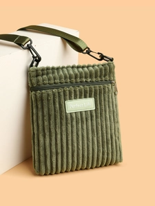 Detail of dark green corduroy crossbody bag with zipper and leather brand label