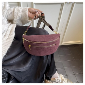 Close-up of burgundy suede saddle bag with dual metal zippers and woven strap