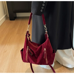 Detail of burgundy suede tote bag featuring golden zippers and side pocket on a model
